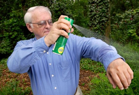 This is an Image of a man spraying repellent on himself.